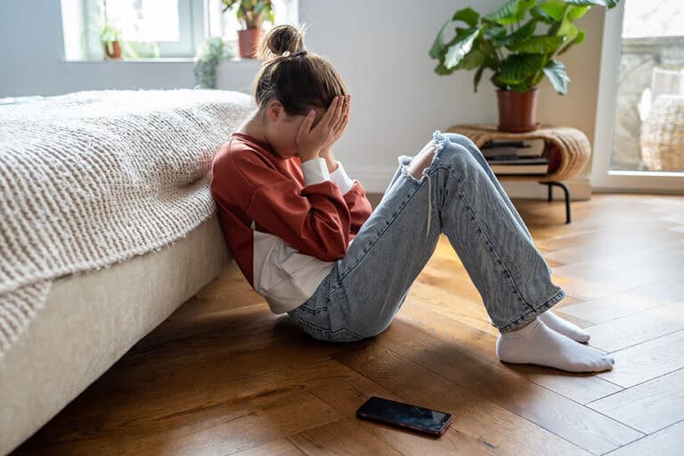 Young teen girl victim of sextortion sitting on floor with face in her hands